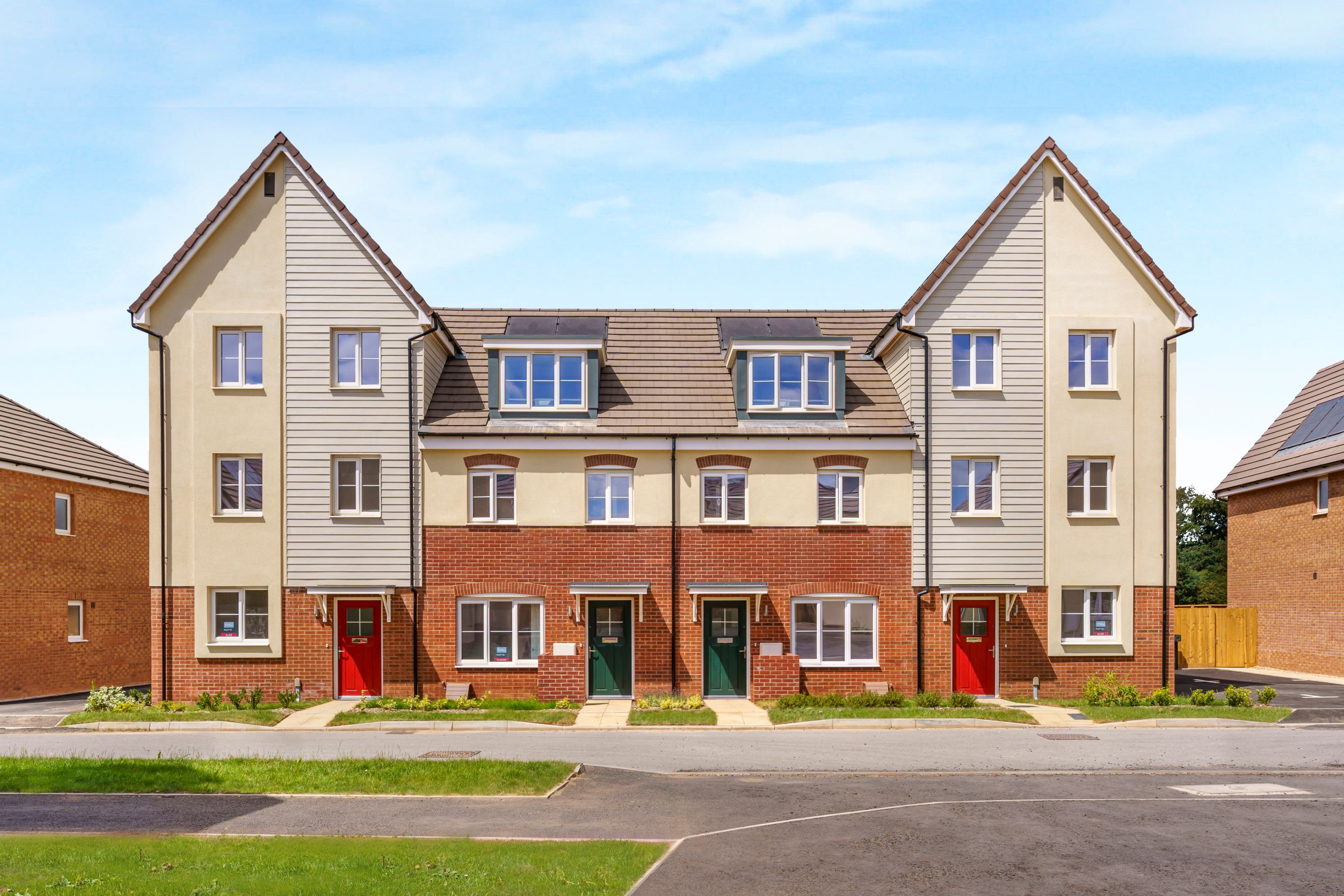 A row of new townhouses with red and green front doors under a blue sky.