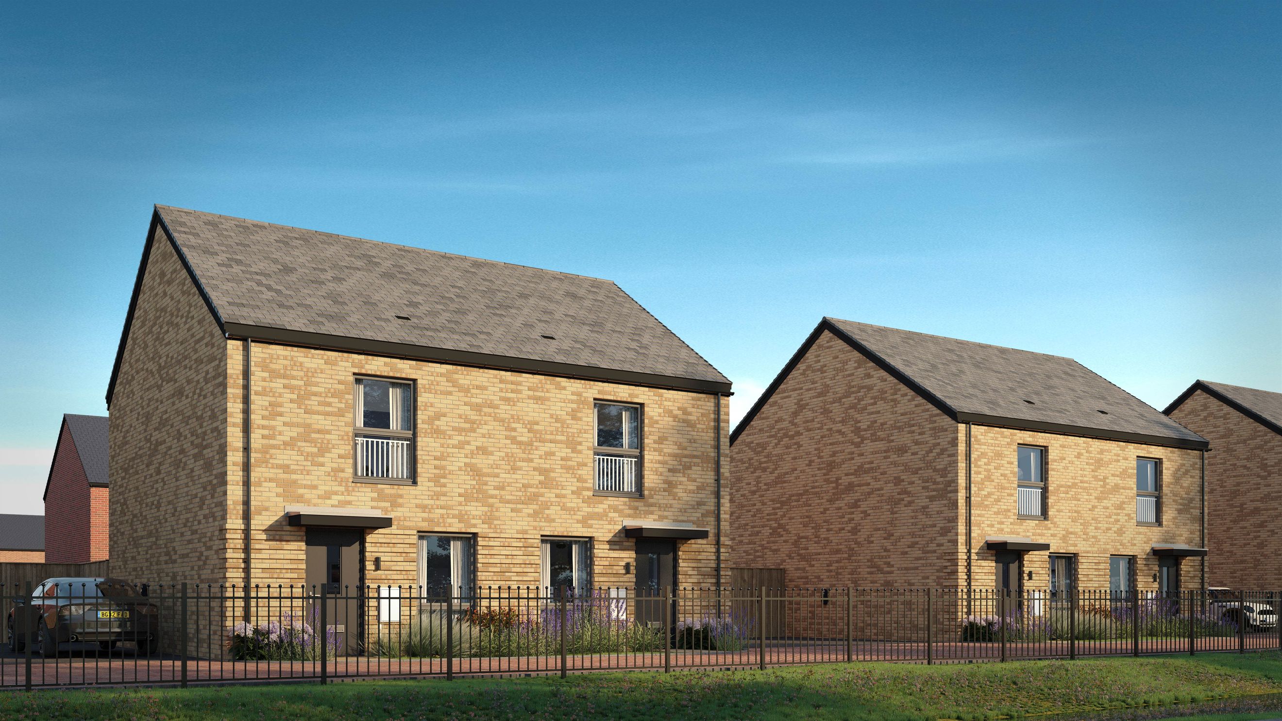 A row of modern brick townhouses with tiled roofs and front gardens behind a black metal fence.