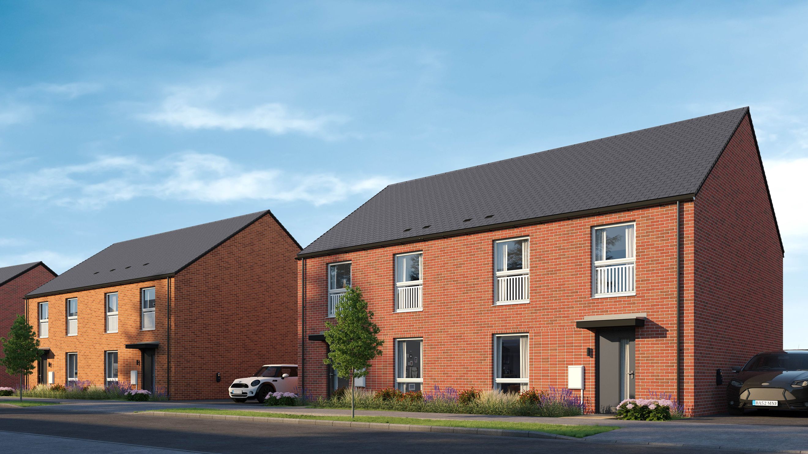 A row of modern red brick houses with dark roofs under a blue sky with clouds.