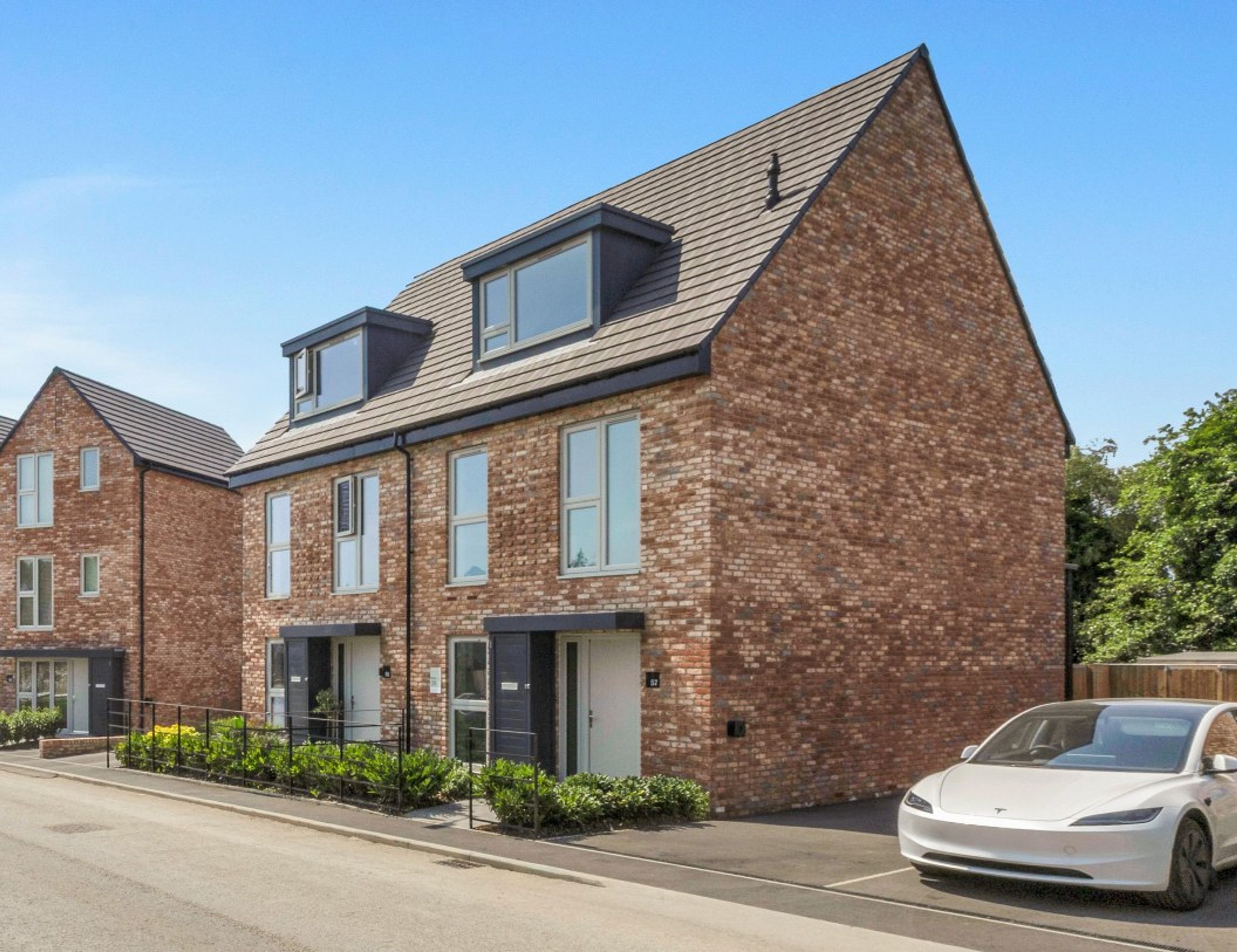 A row of modern brick townhouses with dormer windows and a white electric car parked in the driveway.