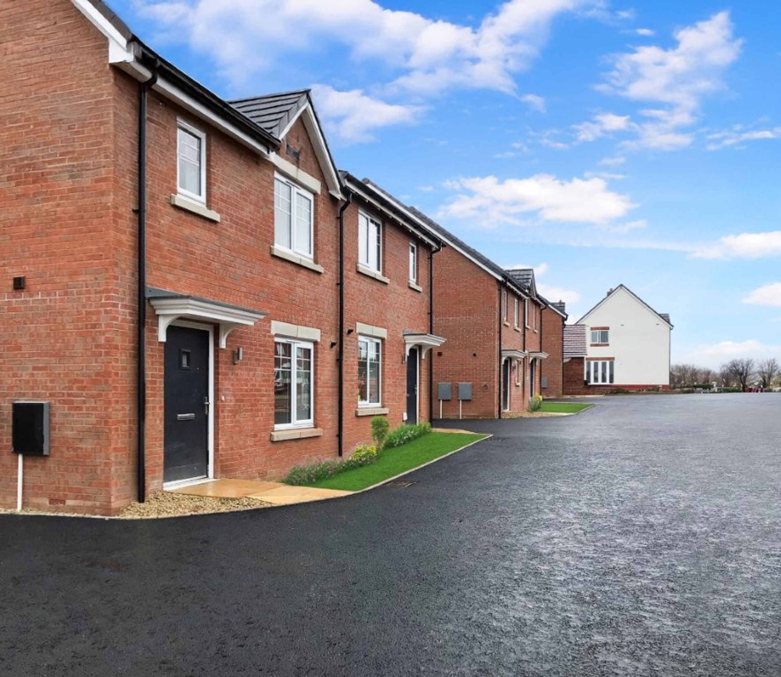 A row of red brick houses with black doors and white windows under a blue sky.