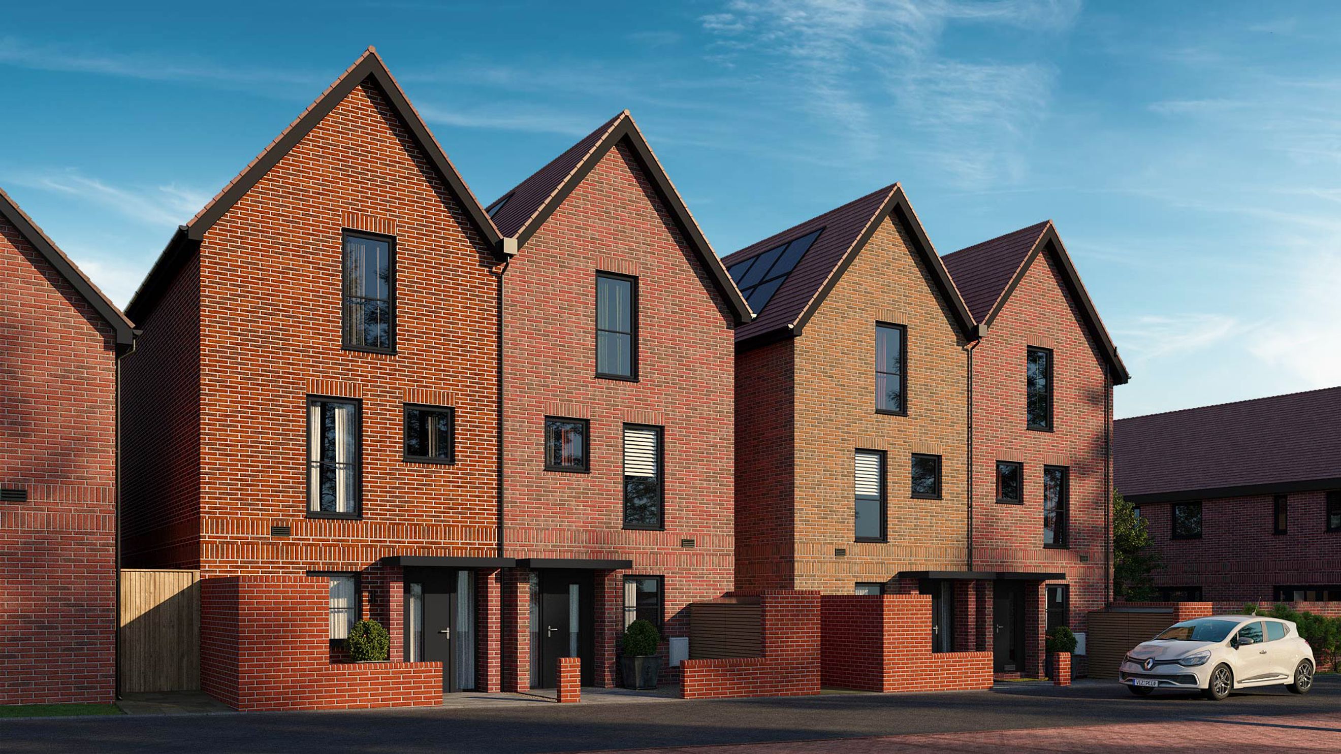 A row of modern red brick townhouses with dark windows and pitched roofs under a blue sky.