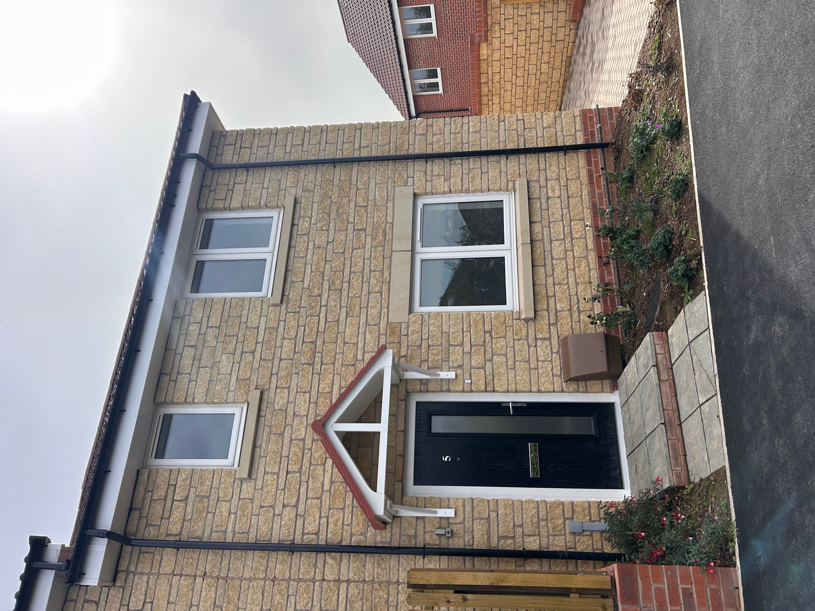 A modern house with a black front door, white-framed windows, and light stone brickwork.