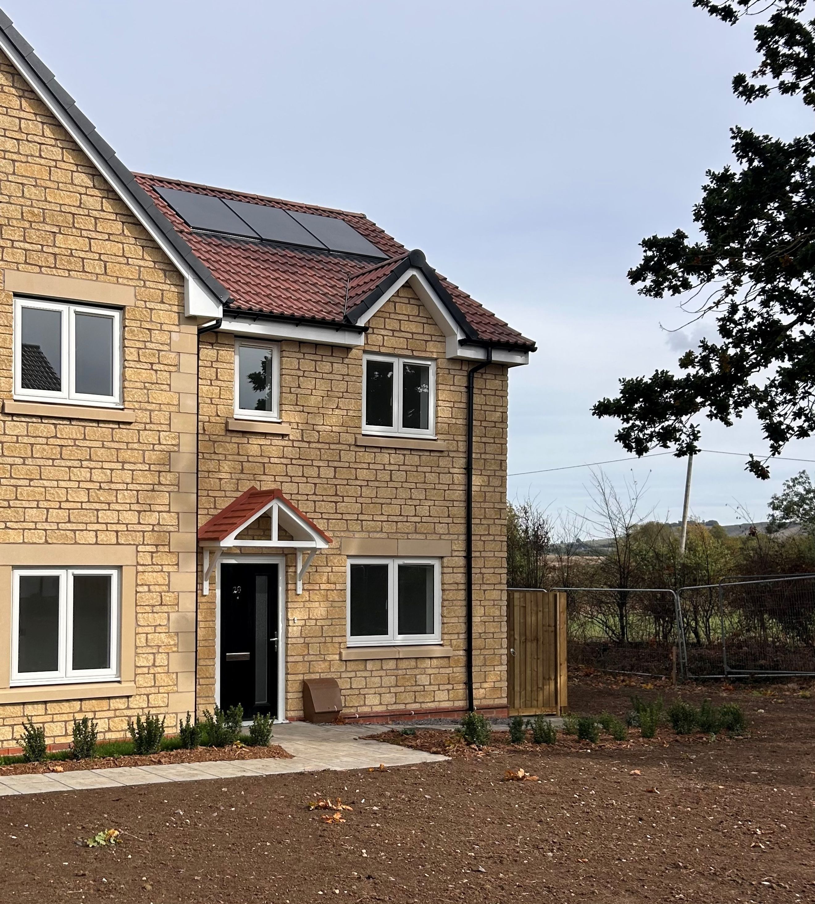 A stone-built house with solar panels on the roof, white windows, and a black front door.