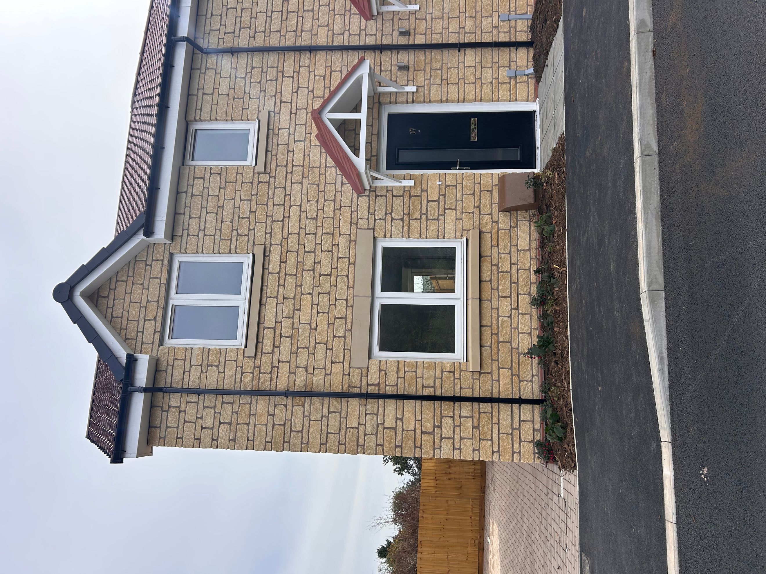 A modern house with a stone facade, black front door, and white-framed windows.