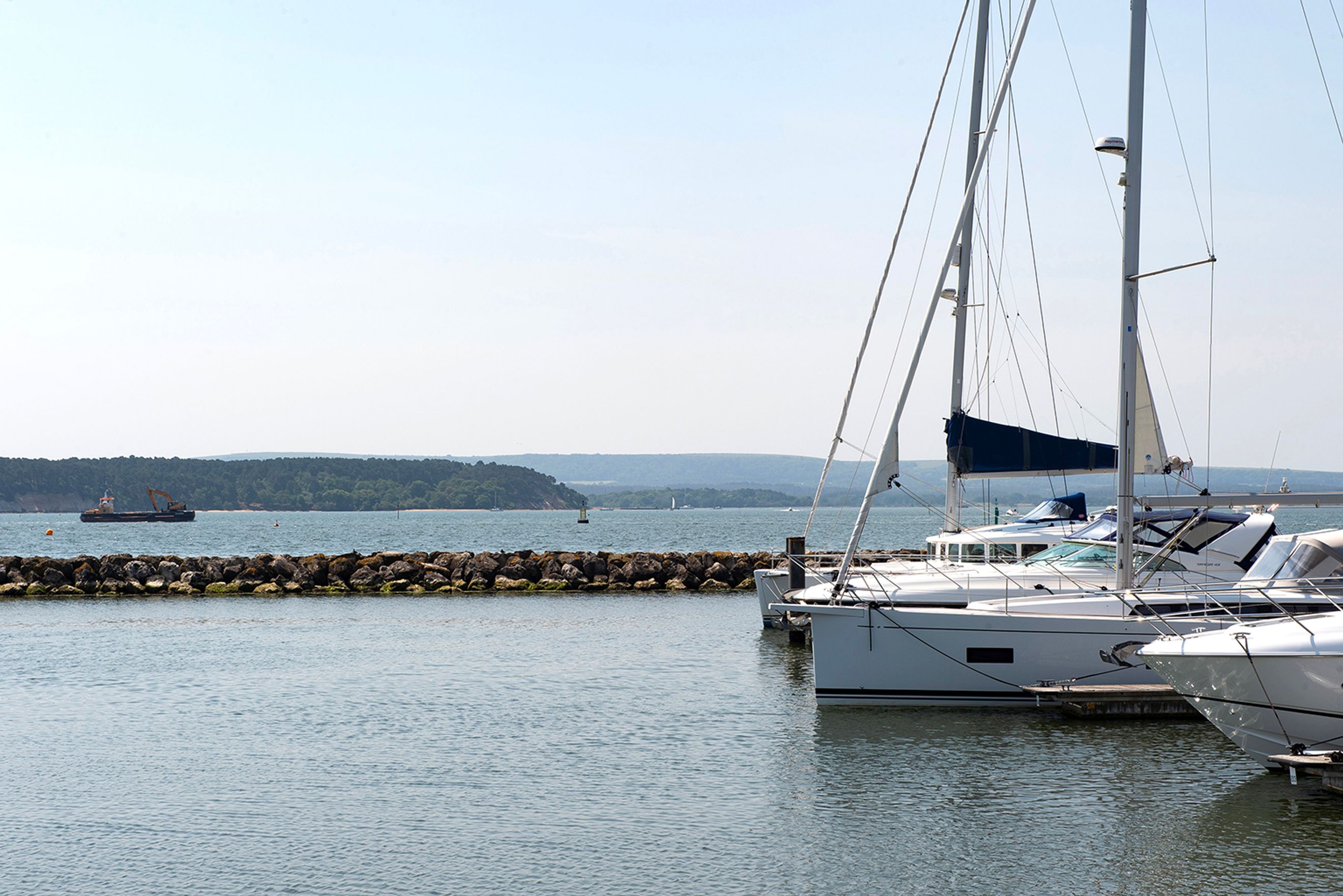 A marina with several sailboats docked and a stone breakwater in the foreground.