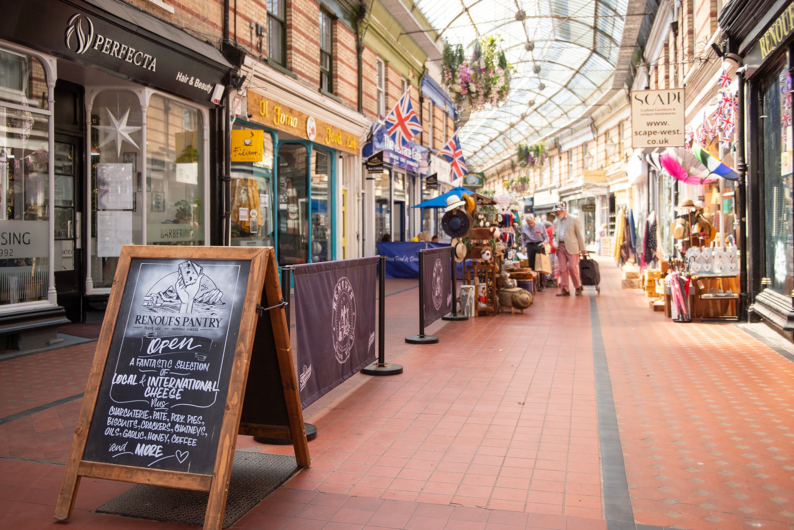 A covered retail arcade with various shops and a chalkboard sign advertising a cheese shop.