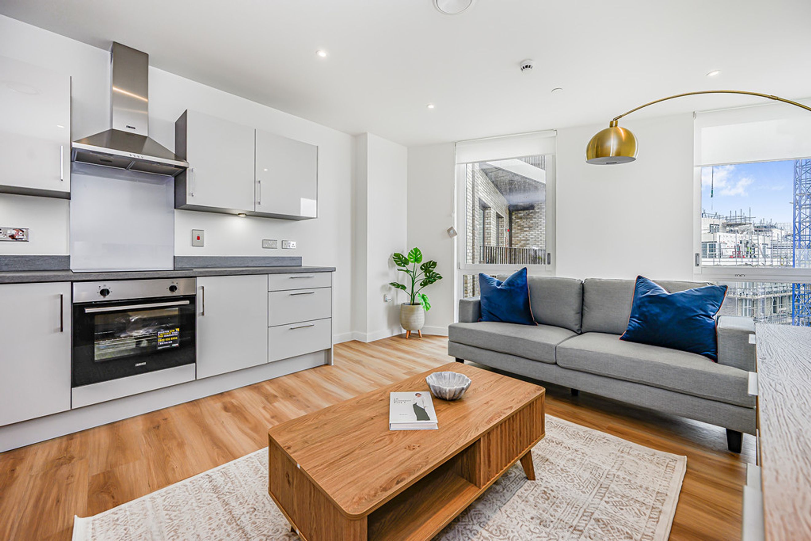 A modern living room and kitchen area with a sofa, coffee table, and kitchen appliances.