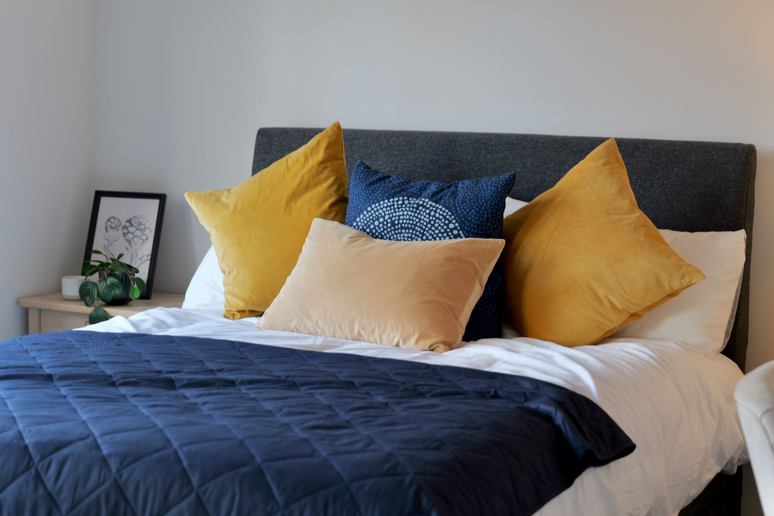 A bedroom with a bed, pillows, and a dark blue quilt.