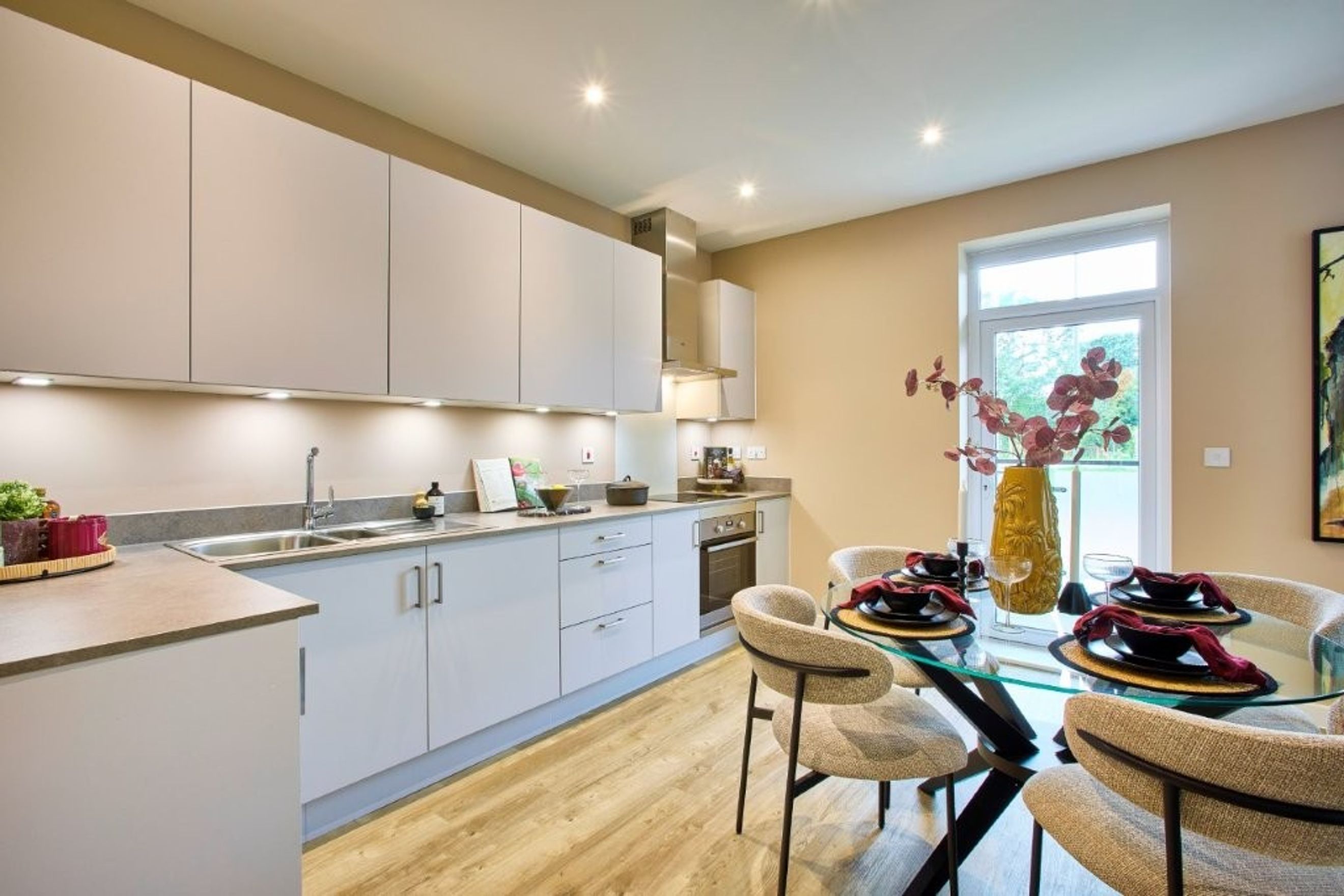 A modern kitchen and dining area with light grey cabinets, a glass-top dining table, and chairs.