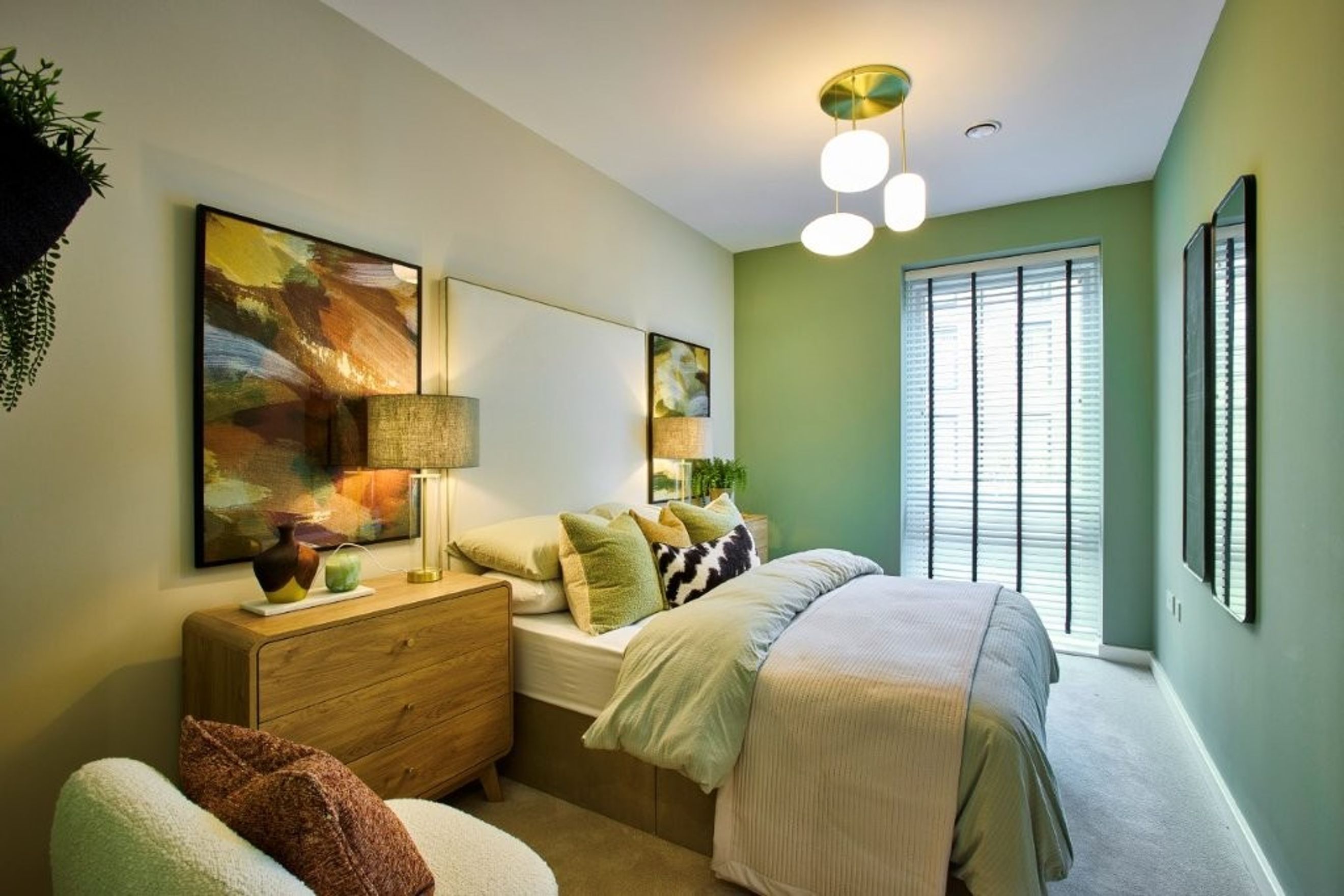 A bedroom with a bed, nightstand, armchair, and abstract art.