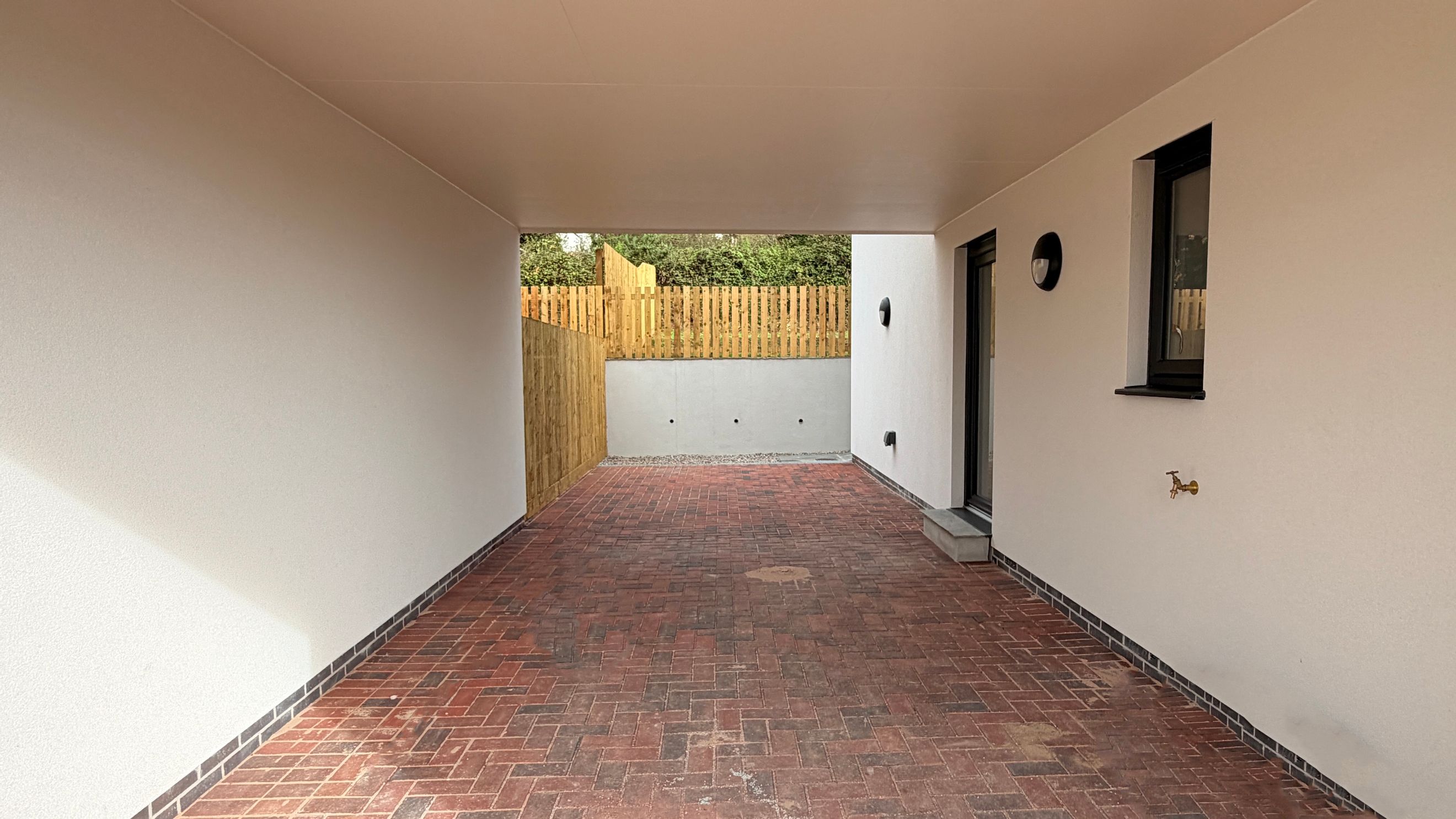 A covered outdoor patio area with brick pavers and white walls.