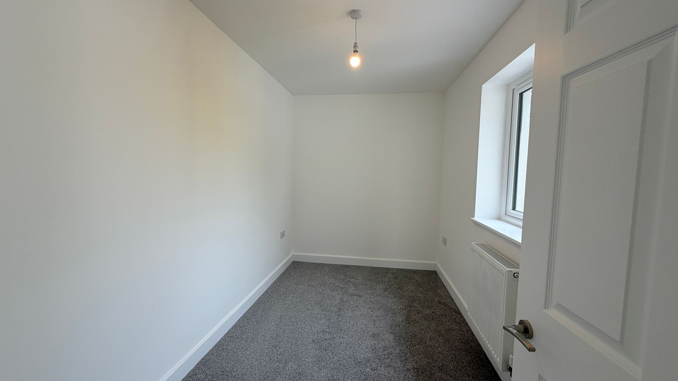 A room with white walls, a grey carpet, a window, and a radiator.