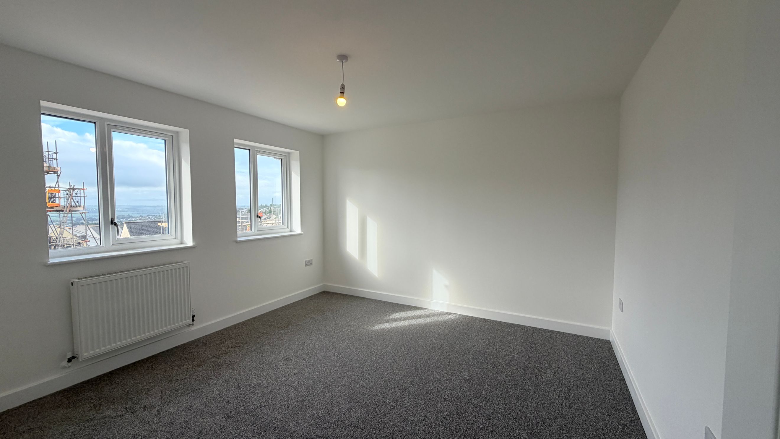 A bedroom with two windows, a radiator, and grey carpet.