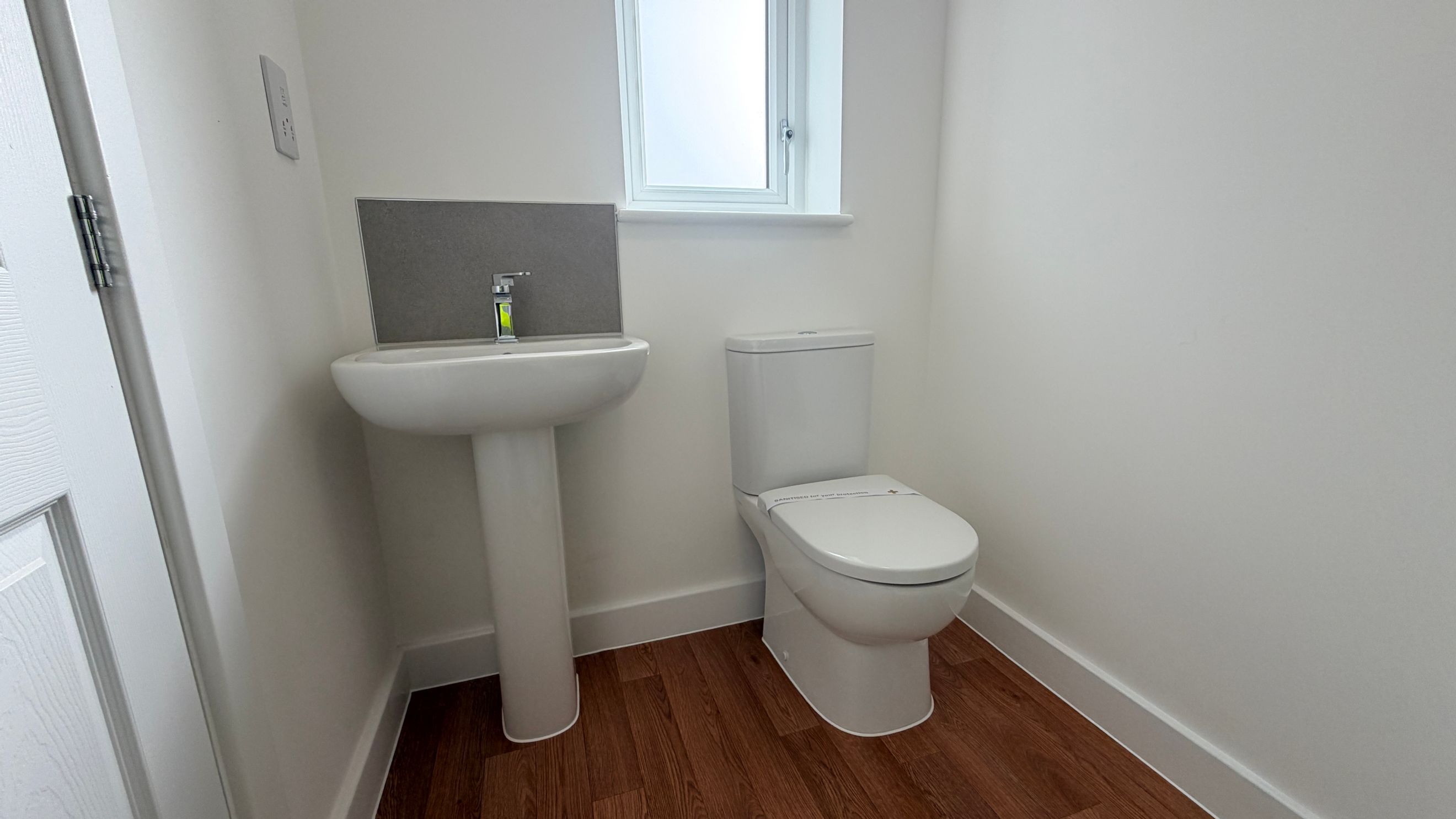 A bathroom with a pedestal sink, a toilet, and a window.