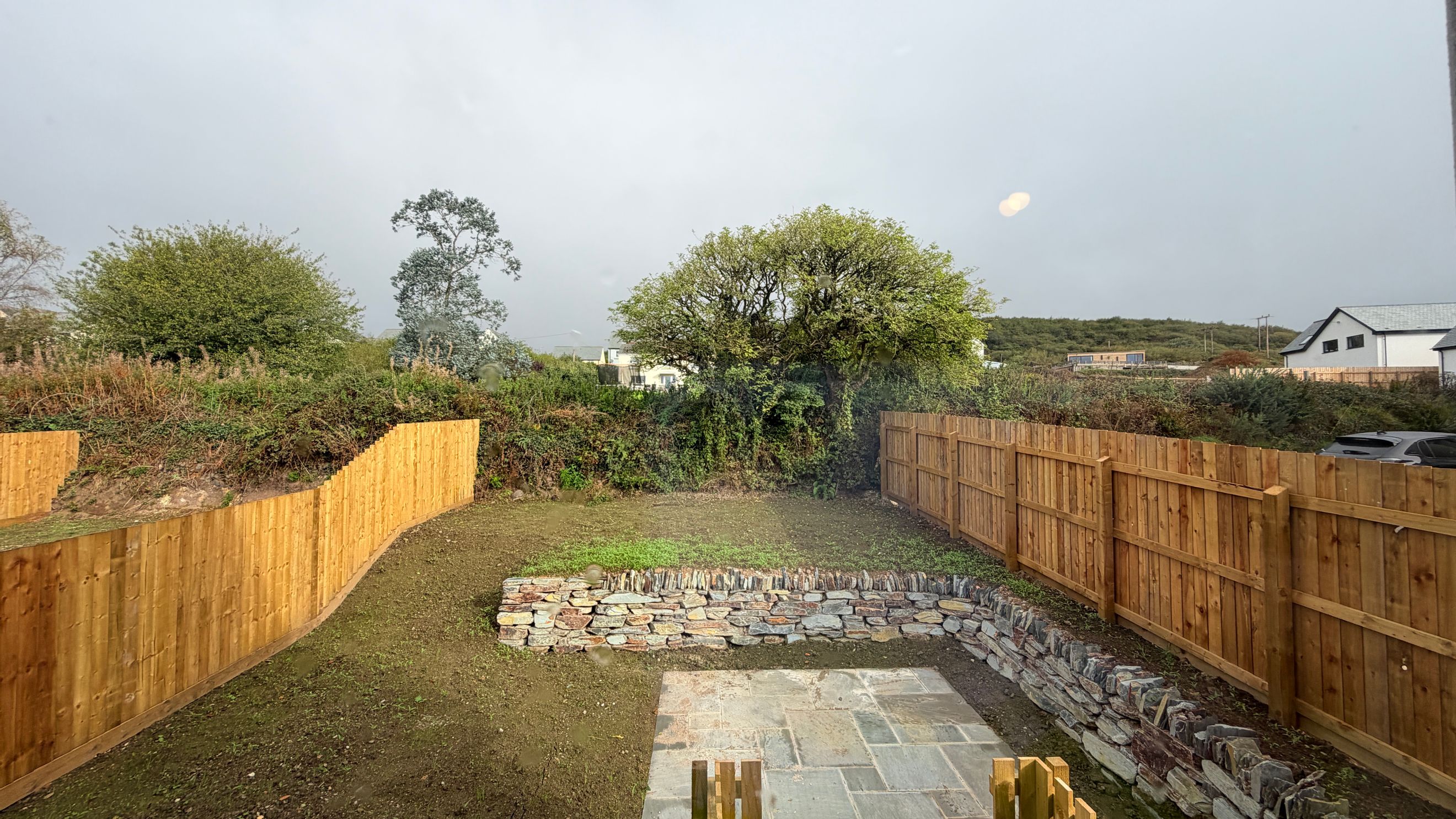 A backyard with a wooden fence, stone wall, and paved patio.