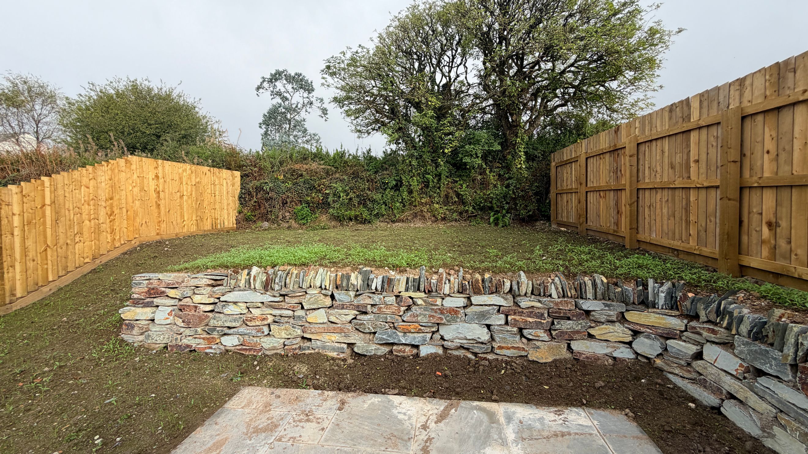 A garden with a stone retaining wall and wooden fences.