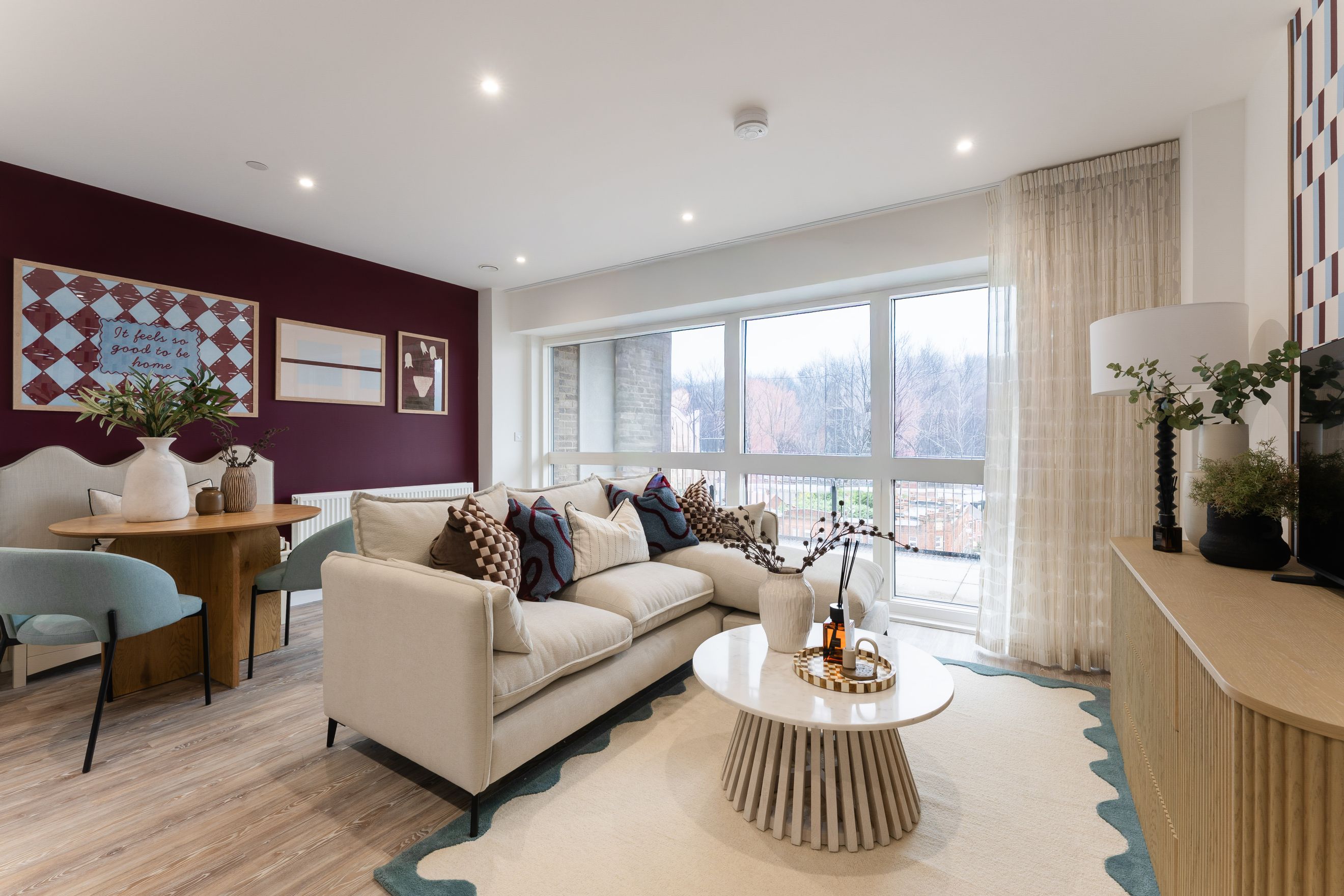 A living room with a sectional sofa, coffee table, dining table, and large windows.