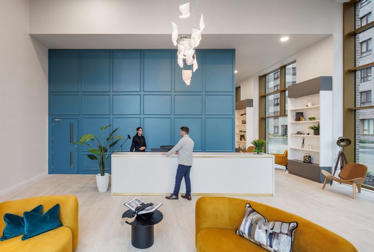 A reception area with a blue wall, white desk, and yellow sofas.