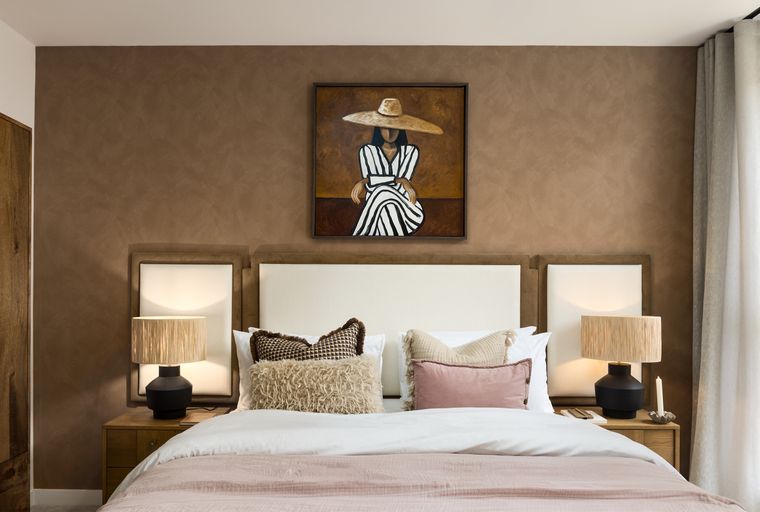 A bedroom with a bed, pillows, lamps, and a painting.