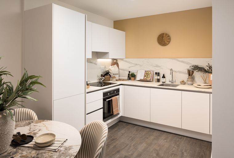 A modern kitchen with white cabinets, a marble backsplash, and a wooden clock on a tan wall.