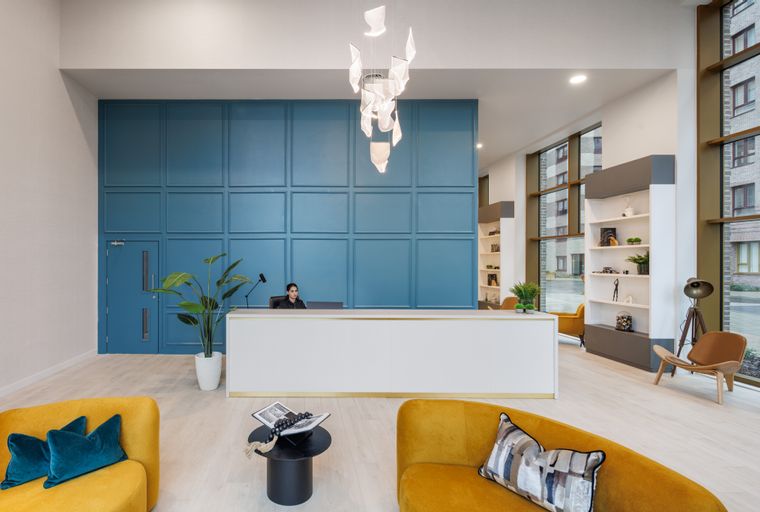 A reception area with a blue paneled wall, white reception desk, and yellow seating.