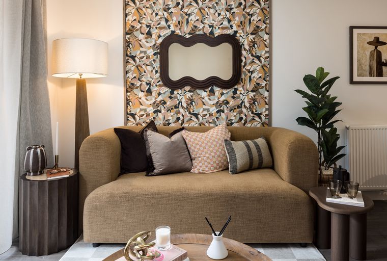 A living room with a sofa, pillows, a floor lamp, and a patterned wallpaper.