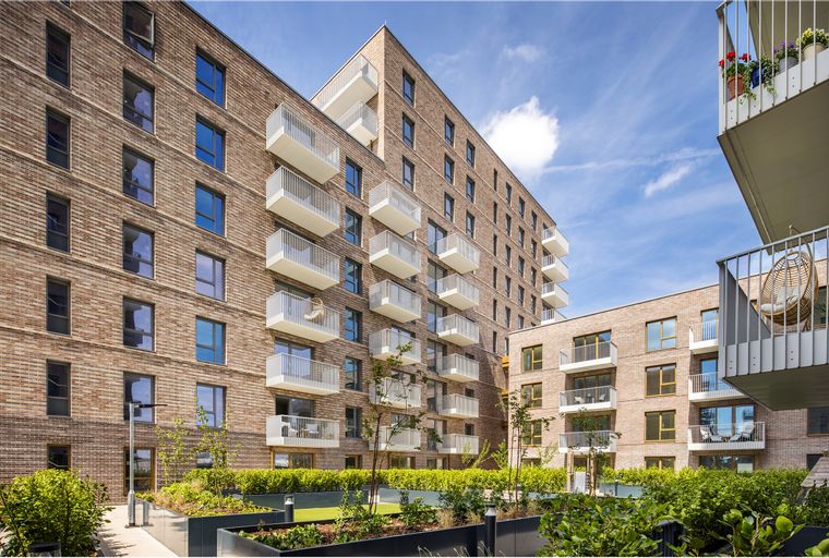 A modern apartment building with brick exterior and white balconies, surrounded by greenery.