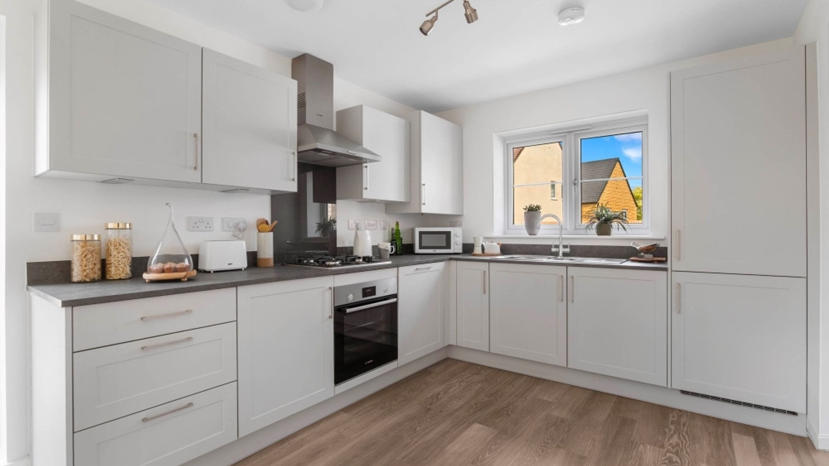 A modern kitchen with white cabinets, grey countertops, and a window.