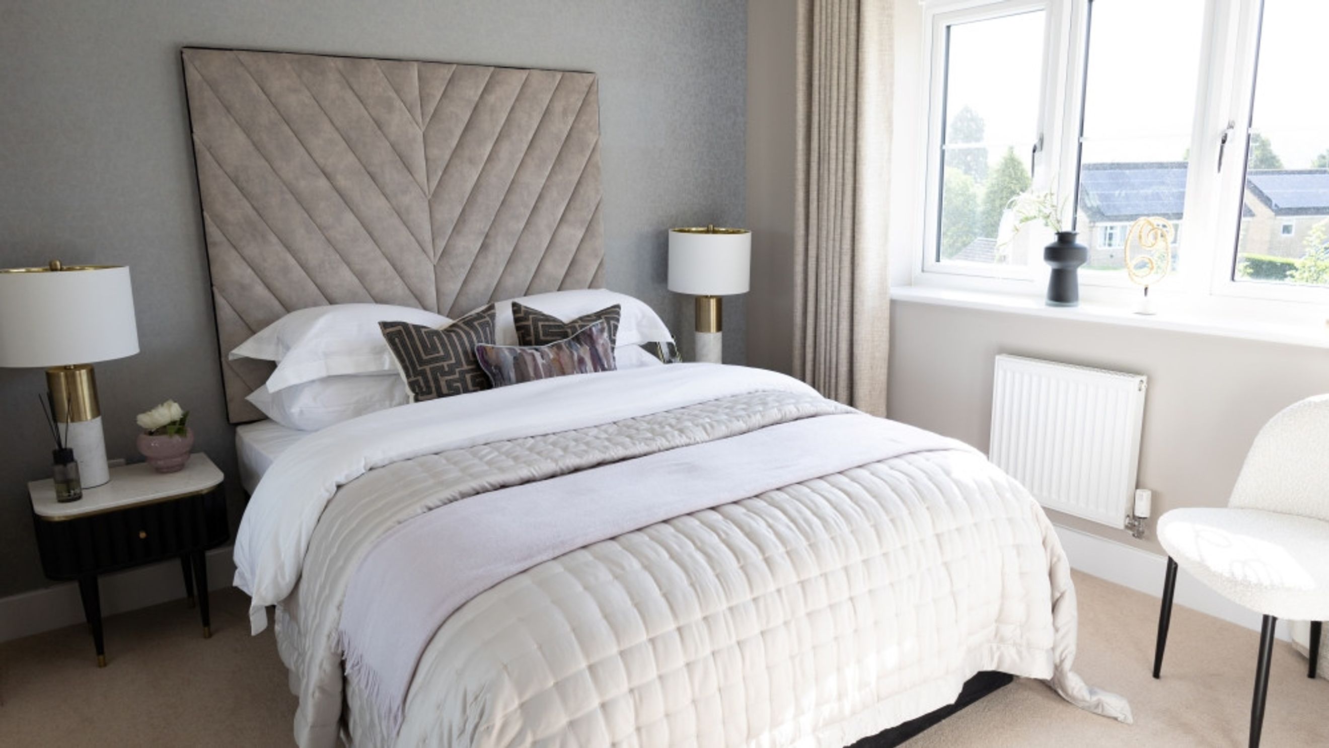 A bedroom with a bed, headboard, bedside table, lamp, and window.