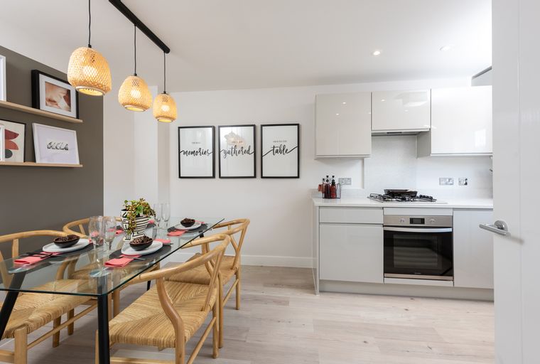 A dining area and kitchen with a glass table, chairs, pendant lights, and modern kitchen cabinets.