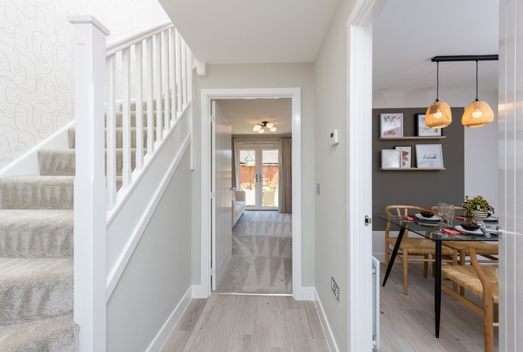 A hallway with a staircase, an open doorway to a living room, and a dining area.
