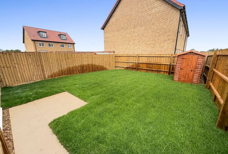 A backyard with a lawn, a patio, a shed, and a fence.