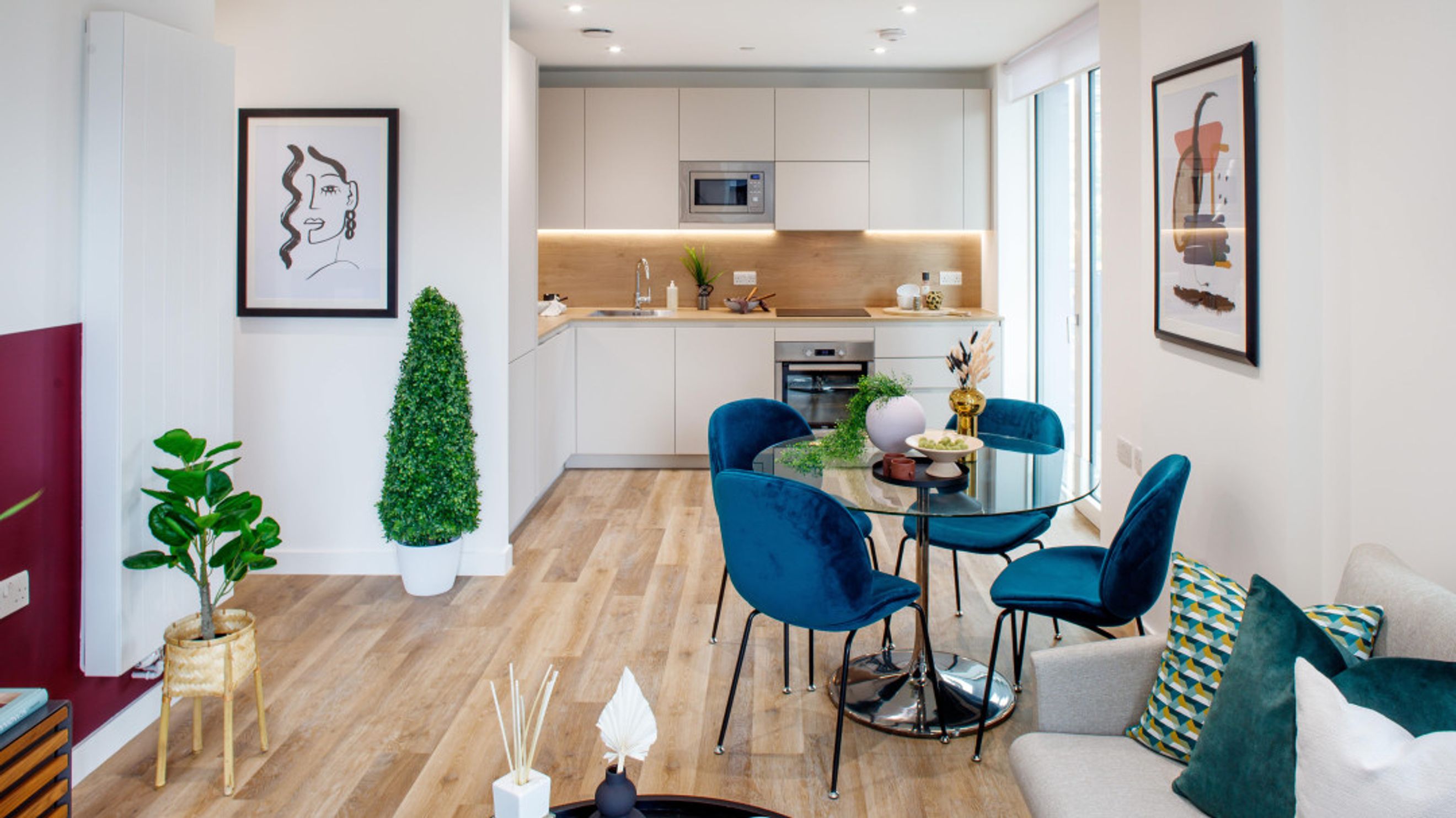 A dining area and kitchen with blue velvet chairs around a glass table.