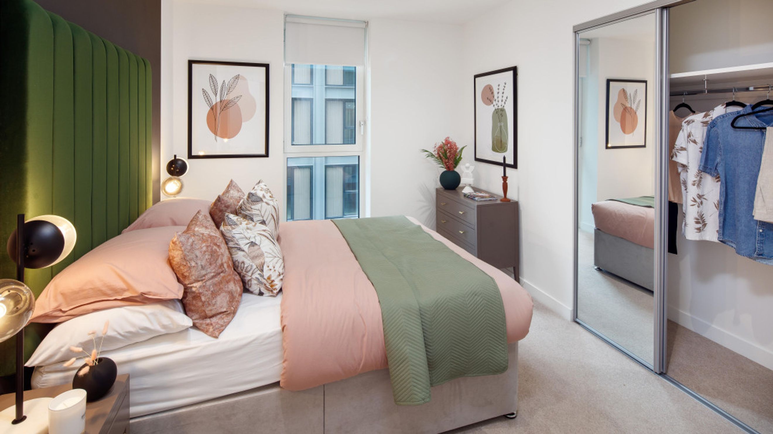 A bedroom with a bed, pillows, a headboard, a dresser, artwork, and a mirrored wardrobe.