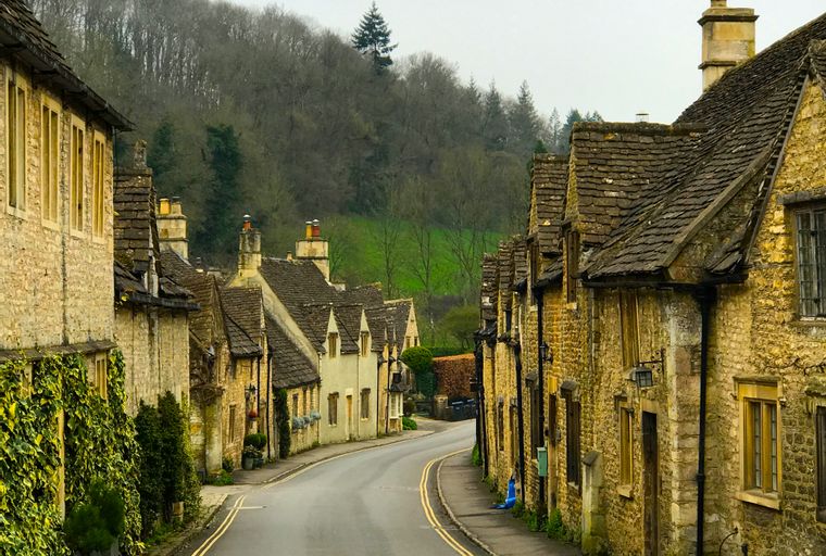 A winding road lined with stone cottages and trees on a hill.