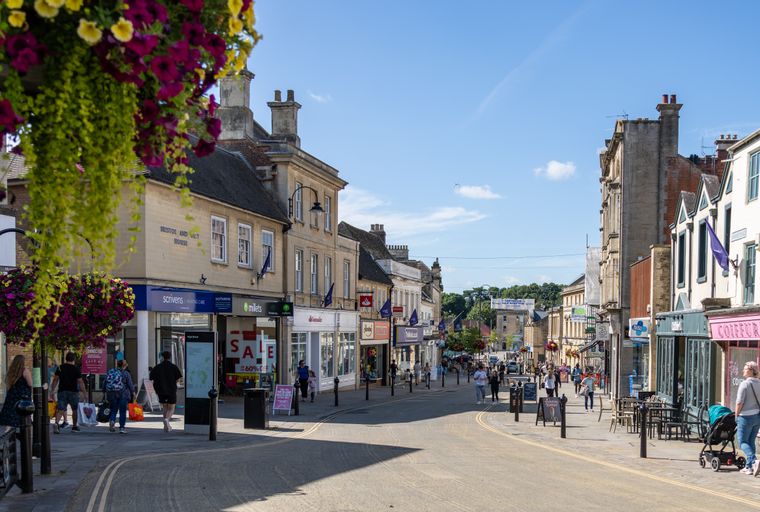 A bustling high street lined with shops and pedestrians on a sunny day.