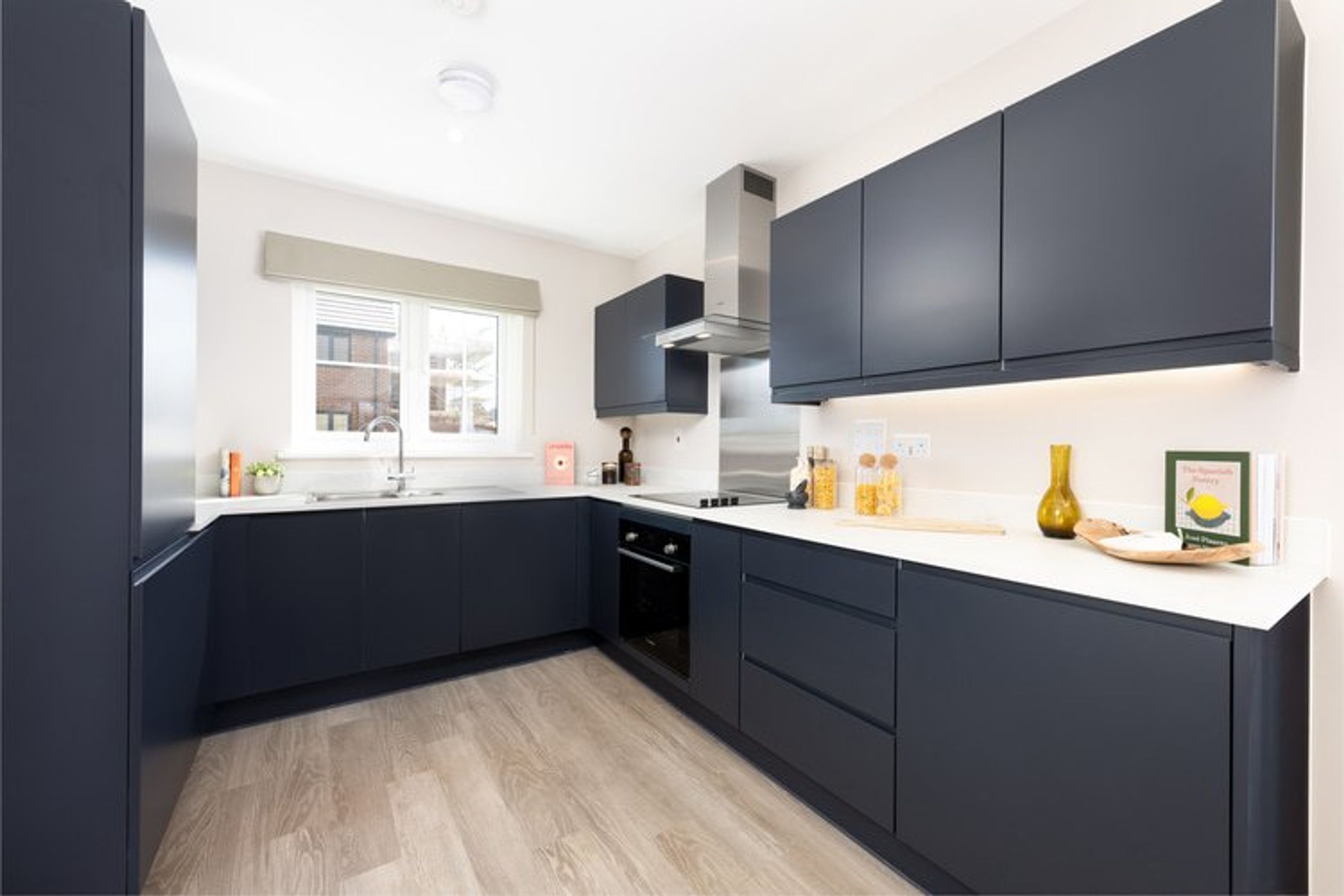 A modern kitchen with dark navy cabinets, white countertops, and a sink under a window.