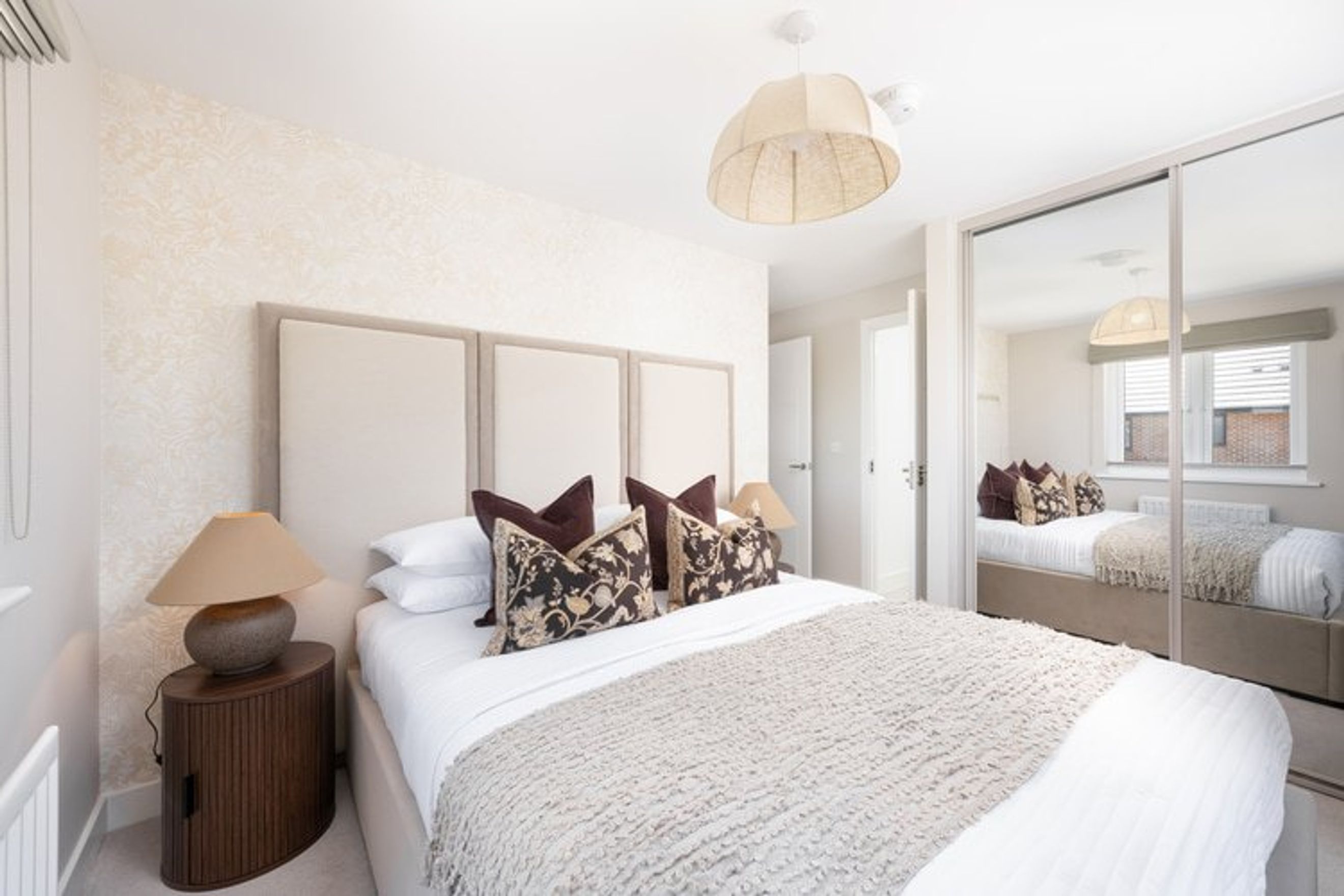 A bedroom with a bed, pillows, a lamp, and a mirrored wardrobe.