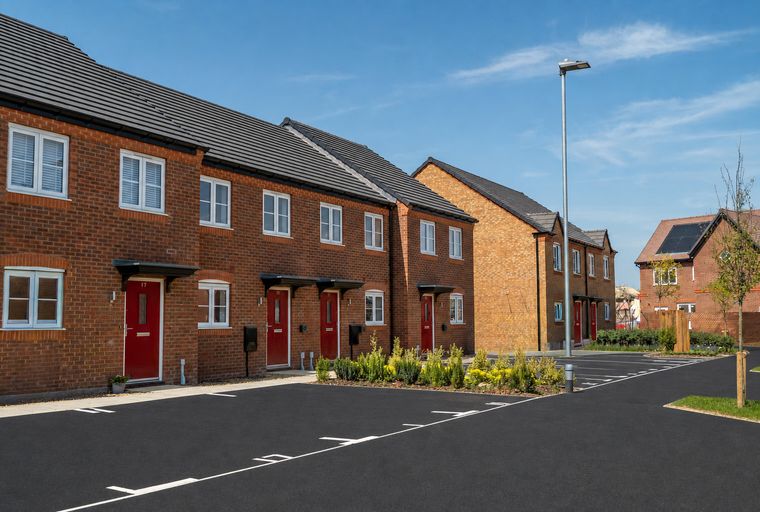 A row of modern brick townhouses with red doors and white windows under a blue sky.