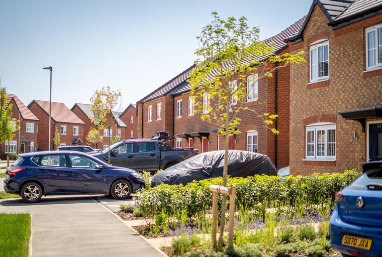 A street view of modern brick townhouses with parked cars and landscaping.