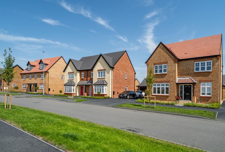A street lined with new houses under a blue sky with scattered clouds.
