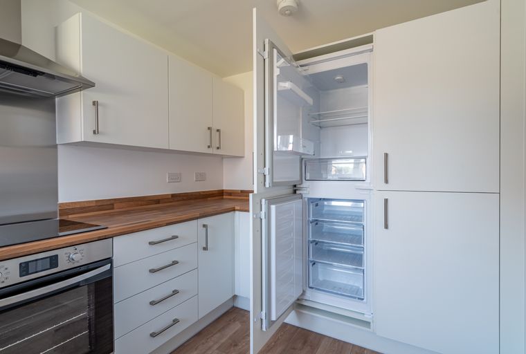 A kitchen with white cabinets, wooden countertops, and an open refrigerator.