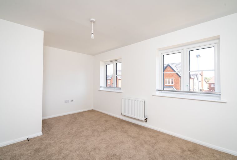 A vacant room with two windows, a radiator, and carpeted flooring.