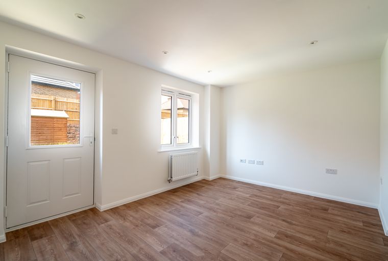 A room with a white door, a window, a radiator, and wood-effect flooring.