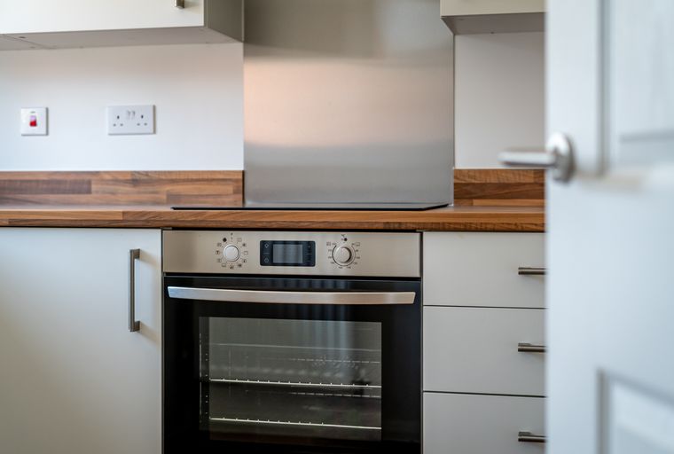 A modern kitchen with a built-in oven, wooden countertops, and white cabinetry.