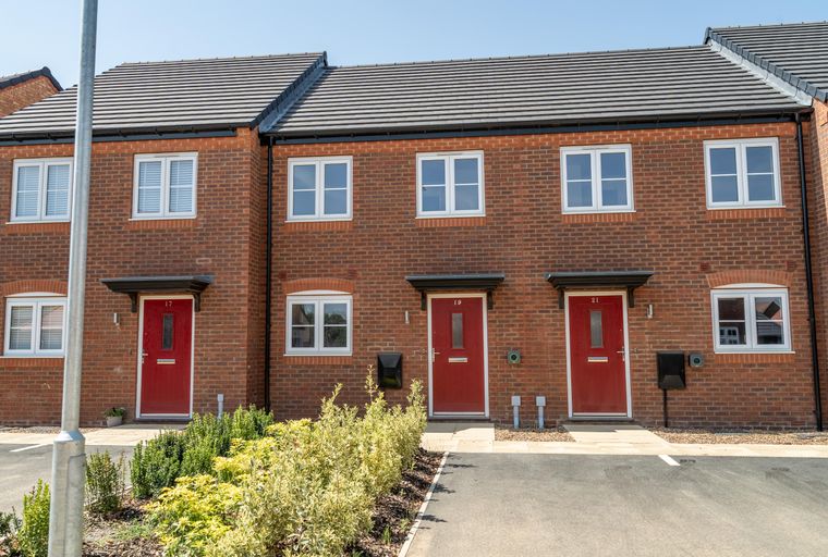 A row of red brick townhouses with red front doors and white windows.
