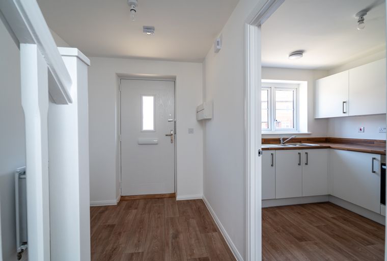 A hallway with a white door and a view into a kitchen.