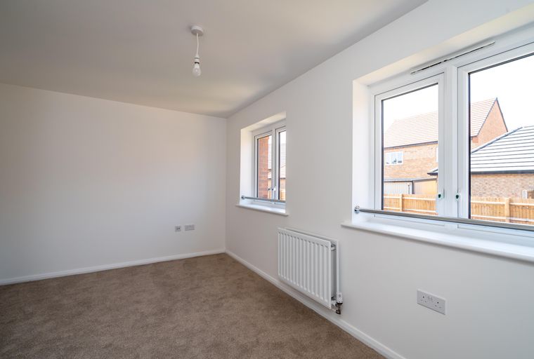 A room with carpet, windows, and a radiator.