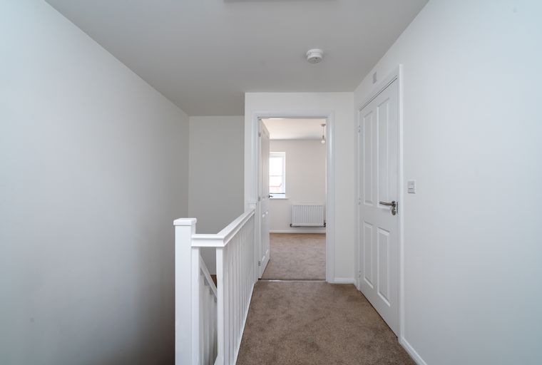 A hallway with a white banister and doors leading to rooms.
